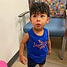 child, toddler, boy, portrait, standing, wide_eyed, surprised, indoors, waiting_room, chair, colorful, polka_dot, blue_shirt, shark, shorts, sneakers, wood_floor, wall, playful, photography