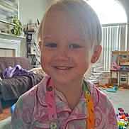 Gracelynn Marie joined the competition — help win amazing prizes! child, toddler, smile, pajamas, lanyard, indoor, living_room, toys, window, natural_light, floor, furniture, blanket, plant, curtains, person, face, happy, hair, home