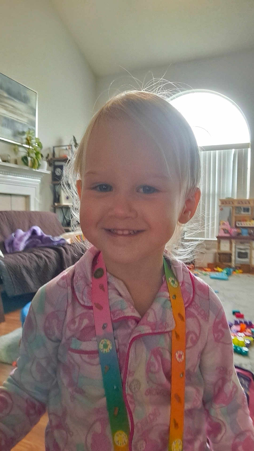 Gracelynn Marie joined the competition — help win amazing prizes! child, toddler, smile, pajamas, lanyard, indoor, living_room, toys, window, natural_light, floor, furniture, blanket, plant, curtains, person, face, happy, hair, home