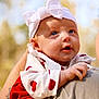 Hailey is registered to the contest to win money with this photo: baby, infant, headband, bow, red_hearts, white_clothing, tattoo, adult_arm, outdoor, nature, portrait, cute, child, holding, person, closeup, happy, smiling, soft_light, skin