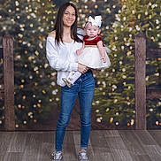 Savanna is registered to the contest to win money with this photo: baby, background, bow, child, christmas_lights, dress, family, fence, festive, glasses, holding, holiday, indoor, jeans, person, portrait, smile, white_sweater, woman, wooden_floor