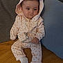 baby, child, hoodie, pink_clothing, socks, couch, pillow, blanket, indoor, infant, cute, seated, face, expression, hand, legs, fabric, pattern, relaxed, home