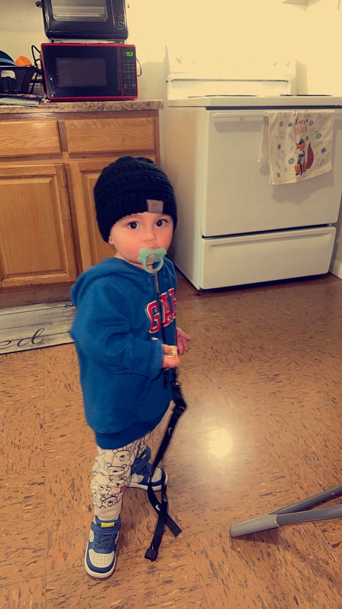 Greyson is registered to the contest to win money with this photo: boot, cabinetry, child, electric_blue, floor, flooring, gas, hat, headwear, home_appliance, human_leg, kitchen_appliance, machine, major_appliance, person, refrigerator, room, sleeve, standing, t_shirt