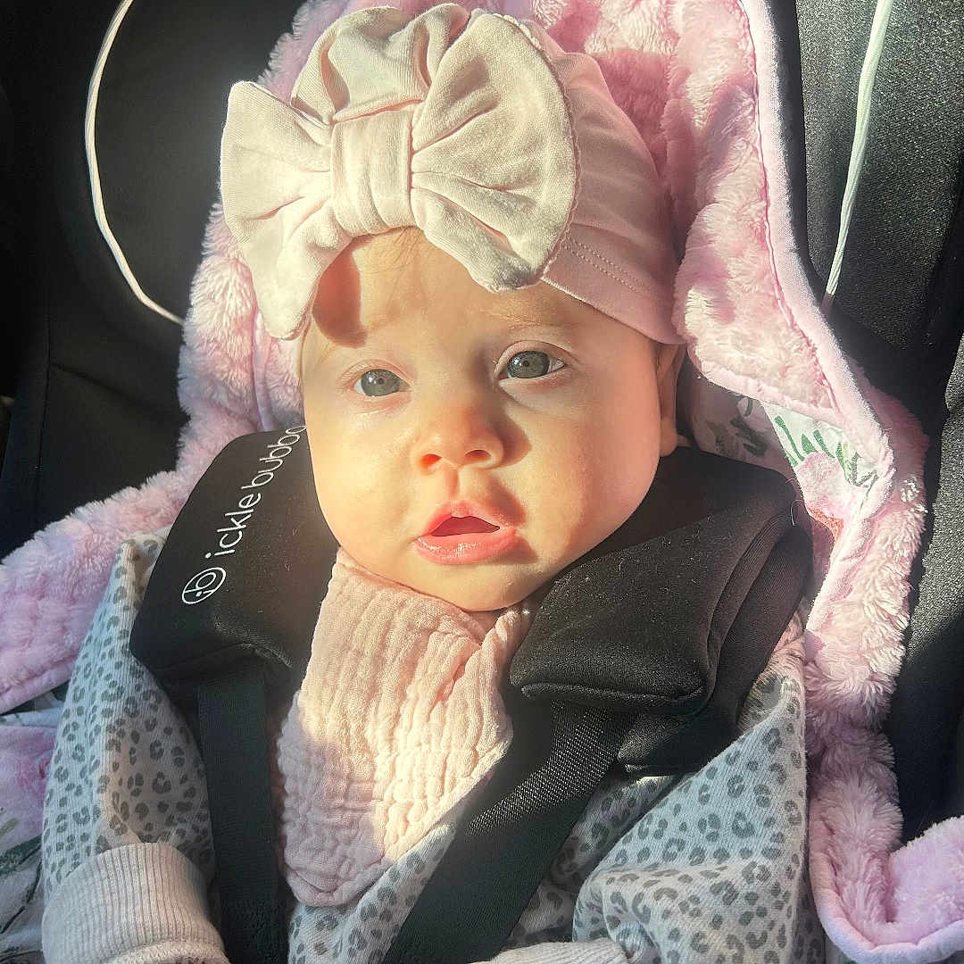 Lexie is registered to the contest to win money with this photo: baby, bonnet, cap, car, car_interior, carseat, clothing, coat, face, hat, head, jacket, knitwear, newborn, person, photography, portrait, sweater, transportation, vehicle