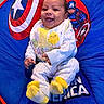 Cristian joined the competition — help win amazing prizes! baby, smiling, child, infant, captain_america, chair, blue, red, yellow, white_clothing, socks, happy, portrait, indoor, cute, seated, person, baby_bib, superhero_theme, colorful