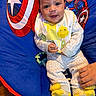 Cristian is registered to the contest to win money with this photo: baby, smiling, child, bib, yellow_socks, captain_america, chair, blue_chair, hand, indoor, cute, clothing, happy, infant, person, comfort, toy, pacifier, colorful, portrait