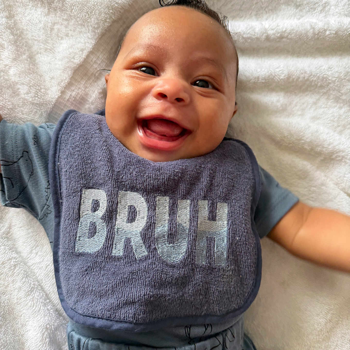 Cristian is registered to the contest to win money with this photo: baby, smiling, bib, towel, happy, infant, clothing, portrait, cute, child, face, expression, laying_down, head, skin, hair, apparel, young_child, one_person, indoor