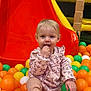 child, toddler, ball_pit, slide, playground, indoor_playground, colorful, orange_balls, yellow_balls, green_ball, white_ball, sitting, portrait, cute, infant, clothing, hand, play, baby, fun