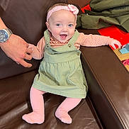Kienna-Jo is registered to the contest to win money with this photo: baby, child, smiling, happy, indoor, couch, leather, hand, clothing, headband, flower, pink, green, tights, person, seated, furniture, adult, watch, skin