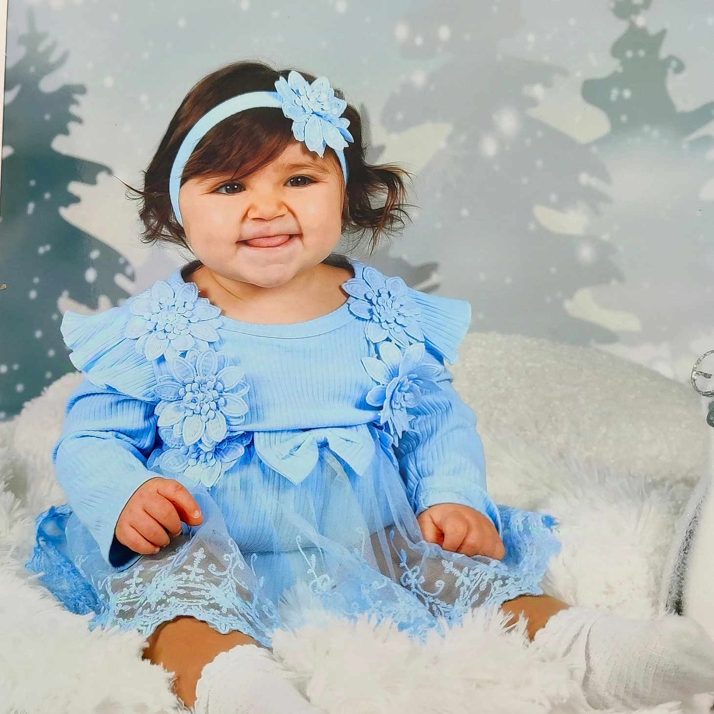 Lara Felgueiras a rejoint le concours — aidez-le/la à gagner de superbes lots ! baby, background, blanket, blue_dress, child, cute, flower, fuzzy_texture, happy, headband, indoor, portrait, sitting, smile, snowflakes, studio_photo, toddler, tongue_out, white_socks, winter_theme
