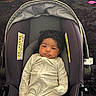 baby, infant, car_seat, onesie, curly_hair, indoor, carpet, toy, child, person, cute, comfort, seat, fabric, clothing, relaxing, home, small, face, young