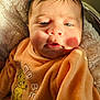 baby, infant, child, face, sweater, orange_clothing, cartoon, lion, text_on_clothing, fluffy_blanket, soft_texture, sunlight, shadow, closeup, portrait, young_child, indoors, cute, warm_light, sleepy
