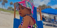 Skai joined the competition — help win amazing prizes! child, toddler, beach, swimsuit, bucket_hat, chair, wood, sky, clouds, outdoor, sunny, sand, vacation, summer, colorful_clothing, person, young_child, playful, holiday, nature