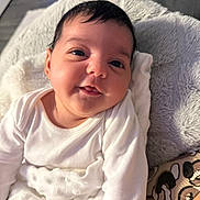 Kumru is registered to the contest to win money with this photo: baby, infant, smile, white_clothing, blanket, couch, indoor, face, child, cute, soft_texture, happy, portrait, young_child, cozy, person, comfort, head, skin, resting