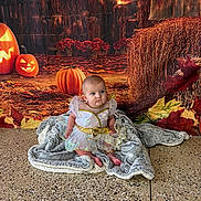 Taylor joined the competition — help win amazing prizes! baby, child, blanket, pumpkin, halloween, fall_leaves, hay_bale, costume, dress, floor, indoor, portrait, cute, festive, seasonal, orange, brown, decor, person, sitting