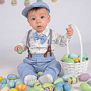 Rocco is registered to the contest to win money with this photo: baby, child, easter_eggs, basket, blue_clothing, cap, suspenders, bow_tie, studio_background, colorful, decorations, holiday, celebration, sitting, cute, portrait, indoor, festive, toys, smiling