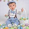 baby, child, easter_eggs, basket, blue_clothing, cap, suspenders, bow_tie, studio_background, colorful, decorations, holiday, celebration, sitting, cute, portrait, indoor, festive, toys, smiling