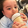 Issa is registered to the contest to win money with this photo: baby, bottle, milk, close_up, child, cute, hand, face, blue_clothing, indoor, portrait, feeding, young_child, infant, skin, eyes, fingers, soft_lighting, cozy, sleepwear