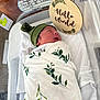 newborn, baby, hospital, bassinet, blanket, green_hat, sleeping, sign, leaf_pattern, hospital_bed, infant, swaddle, peaceful, cute, baby_boy, birth_details, medical, soft, resting, portrait