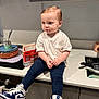 toddler, child, kitchen, counter, white_tshirt, navy_leggings, sneakers, sitting, face, hair, modern_kitchen, curious, food_on_mouth, domestic, indoor, person, young_child, footwear, cute, casual_clothing