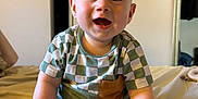 Milo joined the competition — help win amazing prizes! baby, child, smiling, sitting, bed, clothing, green, white, checkered, pocket, room, indoors, happy, face, feet, hands, person, casual, cute, infant