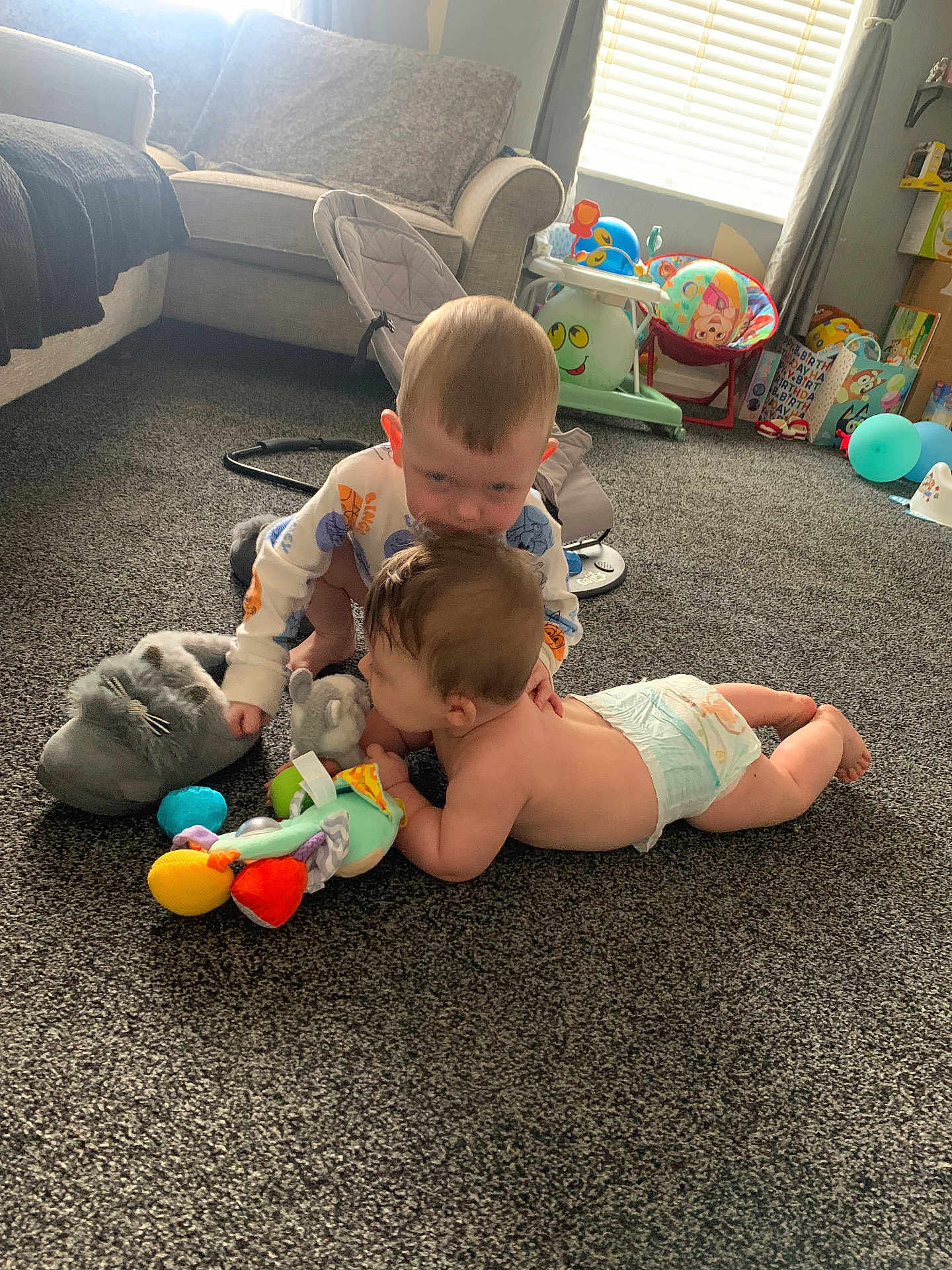 Kyle And Noah is registered to the contest to win money with this photo: baby, toddler, carpet, toy, diaper, living_room, sofa, child, play, floor, cute, home, furniture, stuffed_toy, window, curtain, birthday, balloon, childcare, carpeted_floor