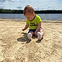 Hunner is registered to the contest to win money with this photo: baby, child, sand, beach, water, lake, sky, clouds, outdoor, sitting, green_shirt, white_socks, nature, daylight, portrait, young_child, casual_clothing, curious, summer, vacation