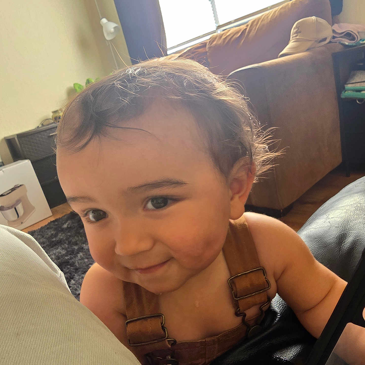 Makai is registered to the contest to win money with this photo: carpet, casual, cheeks, child, closeup, curtains, face, floor, hair, happy, indoors, lamp, living_room, overalls, person, skin, smiling, sofa, toddler, window