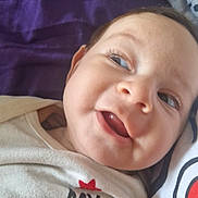 Léa a rejoint le concours — aidez-le/la à gagner de superbes lots ! baby, infant, child, face, smile, gummy_smile, cheeks, eyes, eyelashes, close_up, portrait, onesie, clothing, blanket, purple_background, lying_down, cute, dimple, skin, happy