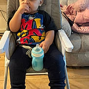 Zayne joined the competition — help win amazing prizes! child, toddler, high_chair, sippy_cup, boots, clothing, indoors, floor, couch, furniture, person, face, hand, sitting, wooden_floor, casual, home, young_child, cute, thinking