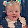 baby, child, smiling, face, car_seat, rainbow, cat_ears, hair_tie, blue_eyes, happy, clothing, seatbelt, infant, cute, indoors, portrait, messy, cheeks, playful, fun