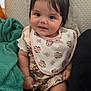 Alaya joined the competition — help win amazing prizes! baby, child, smile, bib, hair_bow, sitting, blanket, clothing, indoor, cute, face, portrait, infant, person, soft_texture, toy_pattern, comfort, happy, young_child, closeup