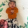 baby, infant, child, lying_down, blanket, headband, cow_print, orange_sweater, pants, tongue_out, cute, smiling, four_month, decor, leaf_pattern, animal_print, cozy, indoor, portrait, playful