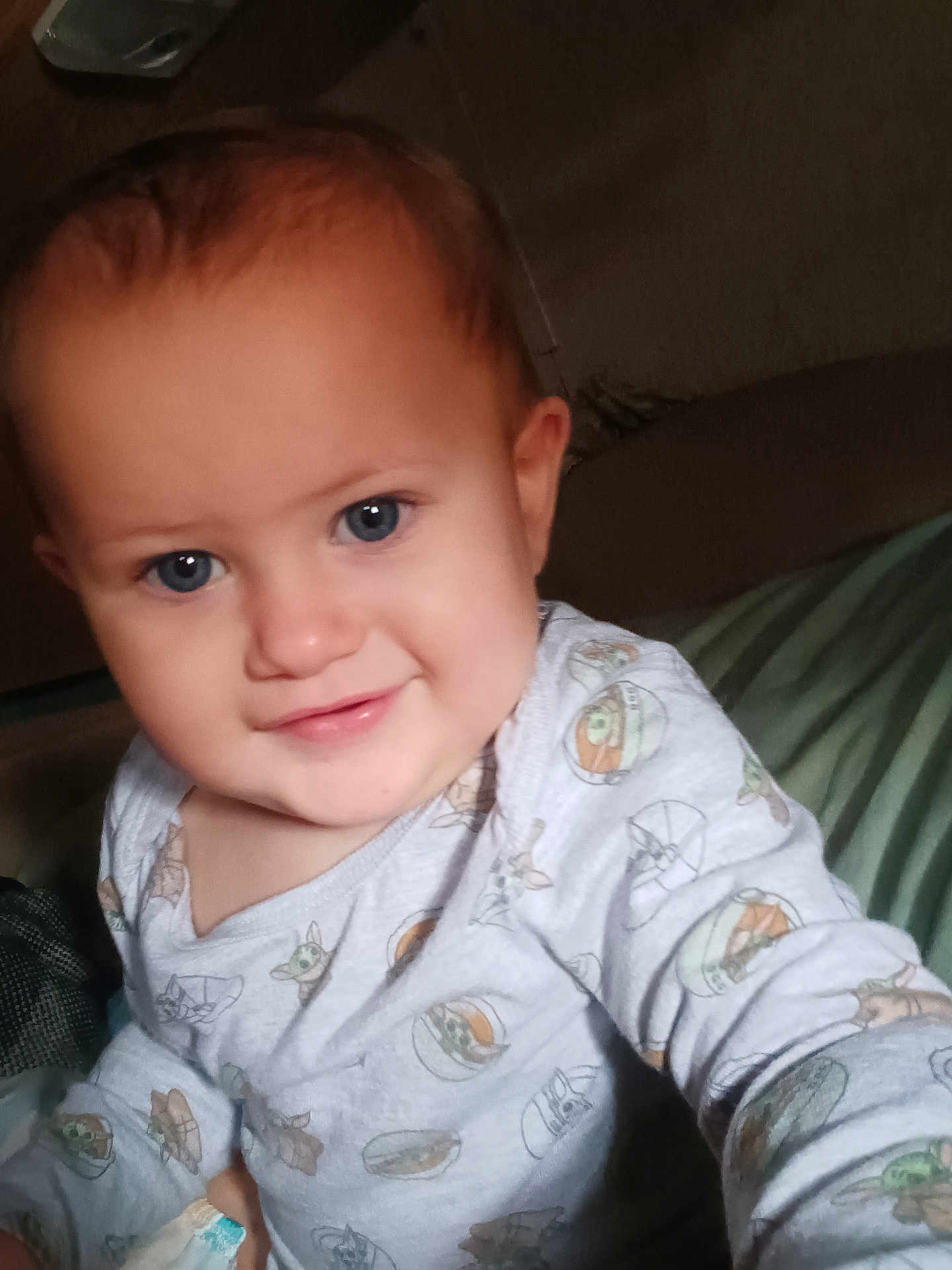Lainey is registered to the contest to win money with this photo: baby, child, face, blue_eyes, smile, onesie, cartoon_print, indoor, couch, seated, cute, infant, young_child, happy, portrait, person, soft_lighting, cozy, playful, casual_clothing