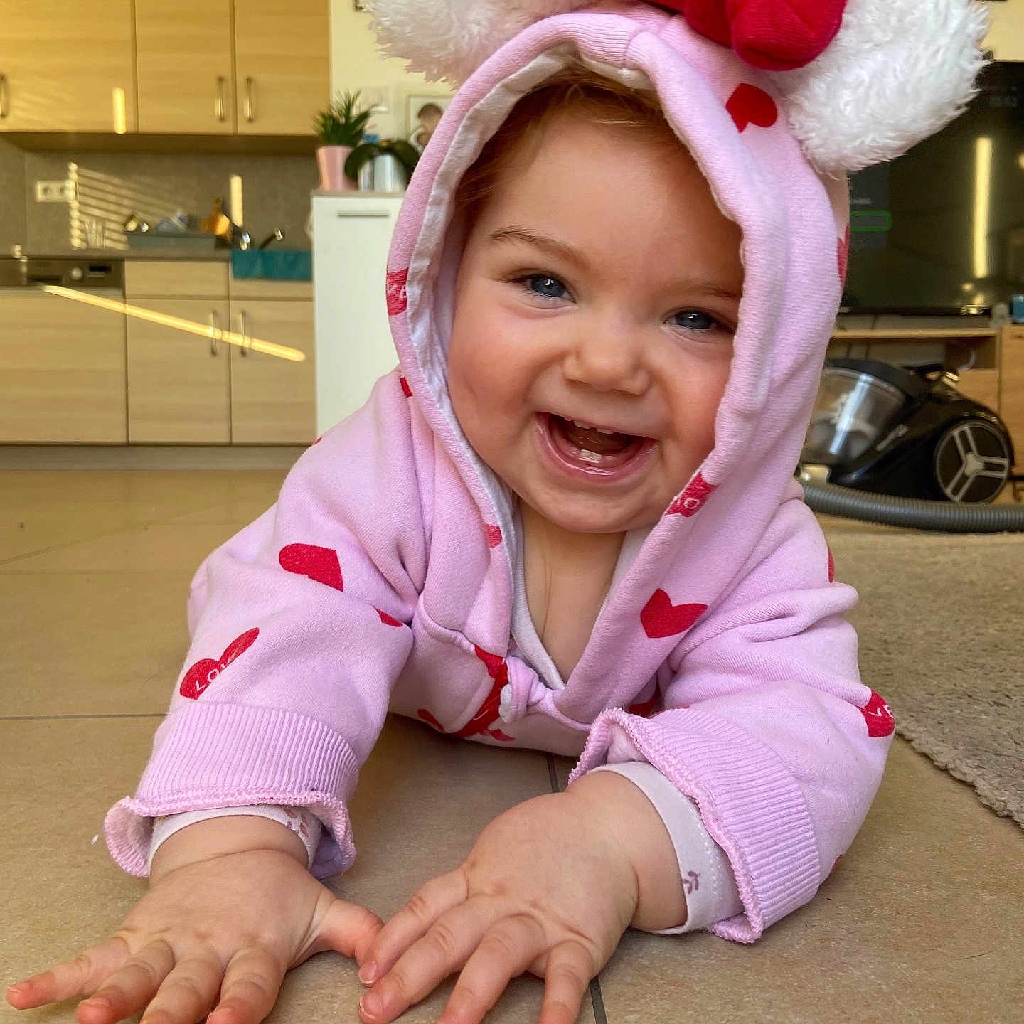 Léna a rejoint le concours — aidez-le/la à gagner de superbes lots ! baby, child, cozy, crawling, cute, face, floor, furniture, hands, happy, home, hoodie, indoor, kitchen, living_room, person, pink_clothing, red_bow, smiling, tile_floor
