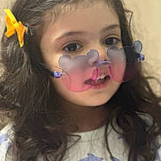 Ayzel joined the competition — help win amazing prizes! accessory, bear_shaped_glasses, child, close_up, curly_hair, cute, dolphin_print, expression, face, fashion, girl, indoors, long_hair, playful, portrait, shirt, smile, soft_background, sunglasses, yellow_bow