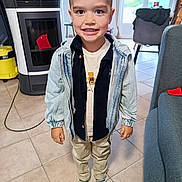 Zak participe au concours pour gagner de l'argent avec cette photo : child, boy, indoor, smiling, standing, denim_jacket, striped_socks, pants, shirt, floor_tiles, living_room, window, chair, stove, natural_light, casual_clothing, young_child, happy, person, home