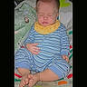 baby, infant, sleeping, sitting, striped_clothing, pajamas, yellow_bib, barefoot, crossed_feet, blanket, quilt, bed, nursery, portrait, indoor, cozy, face, closed_eyes, child, colorful_background