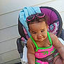 baby, toddler, child, sunglasses, pink, green, seat, straps, curly_hair, smile, outdoor, summer_clothes, playful, cute, portrait, person, fun, colorful, baby_seat, seatbelt