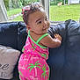 Honesty is registered to the contest to win money with this photo: baby, child, couch, window, greenery, outdoor, indoor, pink_clothing, barbie, sunglasses, smiling, curly_hair, palm_tree_pattern, cushion, home, standing, person, face, happy, playful