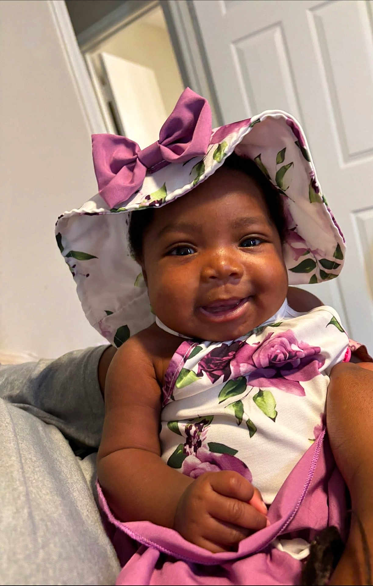 Navonni is registered to the contest to win money with this photo: baby, child, smiling, hat, floral, clothing, indoor, person, cute, portrait, happy, infant, skin, hand, face, headwear, purple, fabric, holding, closeup