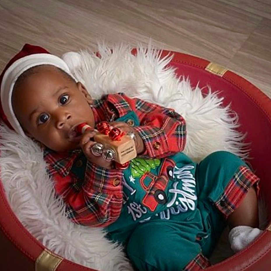 Dale is registered to the contest to win money with this photo: baby, child, santa_hat, christmas_outfit, plaid, red_chair, wooden_toy, bells, curious, indoor, flooring, fluffy_cushion, holiday, festive, cute, infant, portrait, smiling, cozy, relaxing