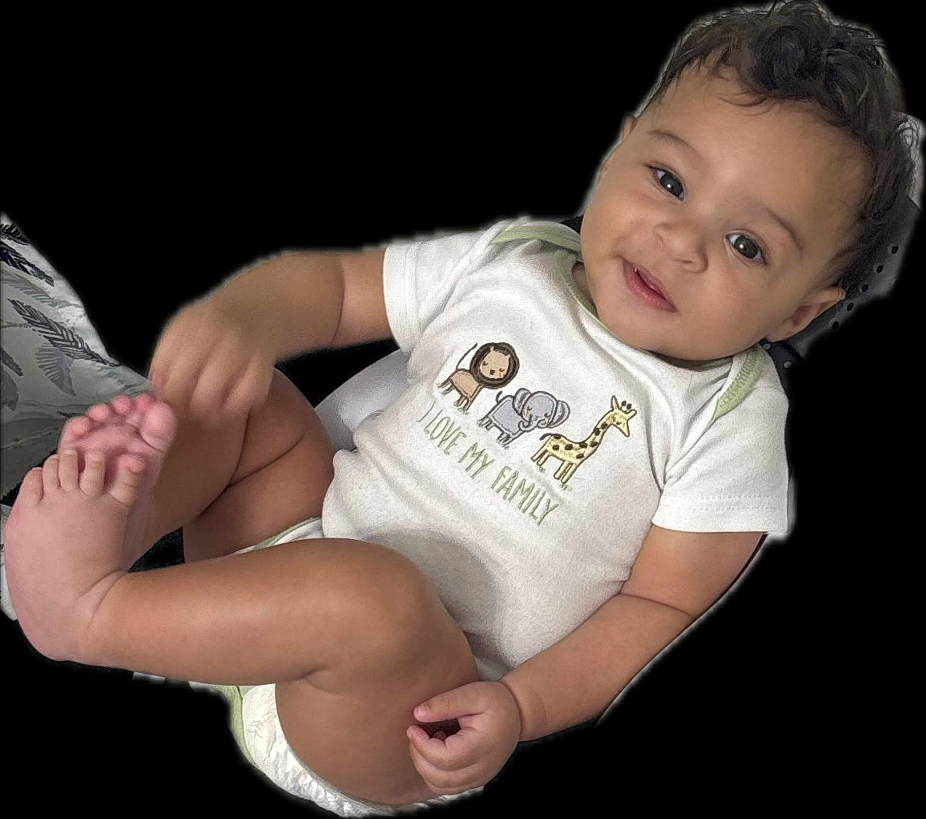 Silas joined the competition — help win amazing prizes! baby, child, onesie, smile, face, foot, hand, animal_print, text_on_clothing, cute, infant, skin, black_background, happy, portrait, sitting, young_child, diaper, playful, casual_clothing