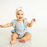 Josie joined the competition — help win amazing prizes! baby, child, smiling, sitting, headband, bow, romper, blue_clothing, barefoot, happy, cute, infant, studio, white_background, arms_outstretched, floor, portrait, playful, chubby_arms, expression