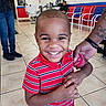 child, boy, smile, barbershop, striped_shirt, tattoo, hand, chair, floor_tiles, interior, person, waiting, mirror, door, poster, casual_clothing, happy, indoor, portrait, haircut