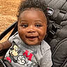 baby, child, smiling, mickey_mouse, stroller, curly_hair, happy, cute, portrait, outdoor, clothing, seatbelt, person, infant, closeup, toddler, black_hair, casual, seat, daylight