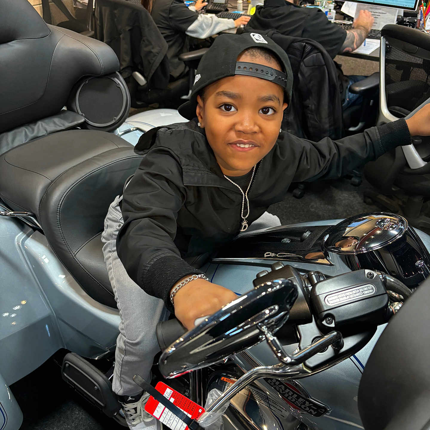 Deandre Jr. joined the competition — help win amazing prizes! black_jacket, bracelet, cap, carpet, casual_clothing, chair, child, computer, desk, handlebars, harley_davidson, indoor, motorcycle, necklace, office, people, playful, reflection, sneakers, young_person