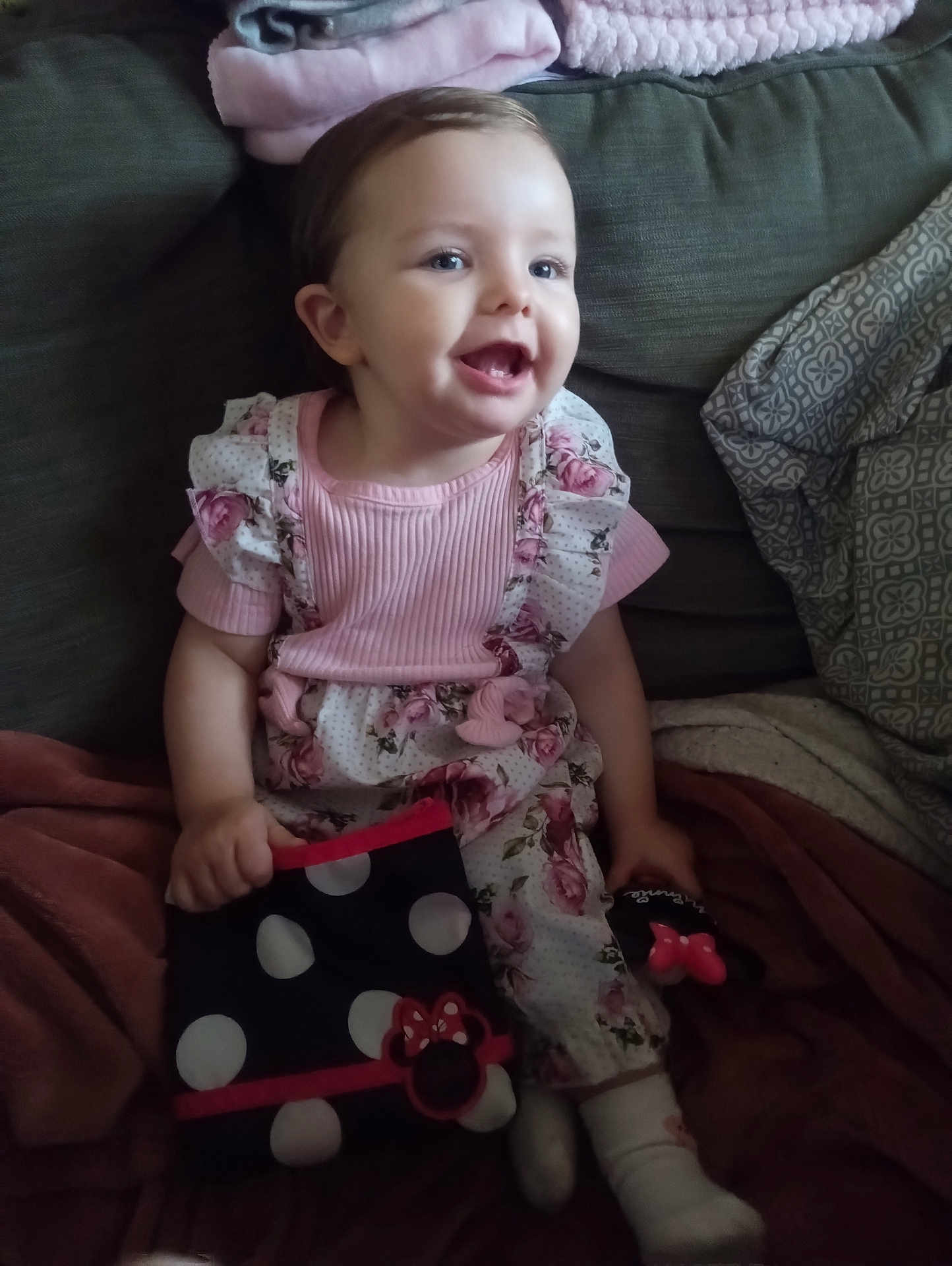 Dakota is registered to the contest to win money with this photo: toddler, child, smiling, pink_clothing, floral_pattern, couch, blanket, polka_dots, pouch, gloves, indoor, happy, cute, baby, person, sitting, toy, cozy, portrait, home
