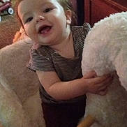 Dakota is registered to the contest to win money with this photo: child, toddler, smile, indoor, toy, rocking_chair, furniture, cozy, happy, person, clothing, carpet, hand, face, hair, room, cushion, plush, wood, baby