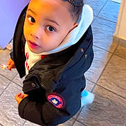 Jayden participe au concours pour gagner de l'argent avec cette photo : child, kid, boy, cornrows, lollipop, black_jacket, hoodie, indoor, tile_floor, curious, looking_up, casual_clothing, portrait, young, person, floor, doorway, purple_wall, winter_wear, cute